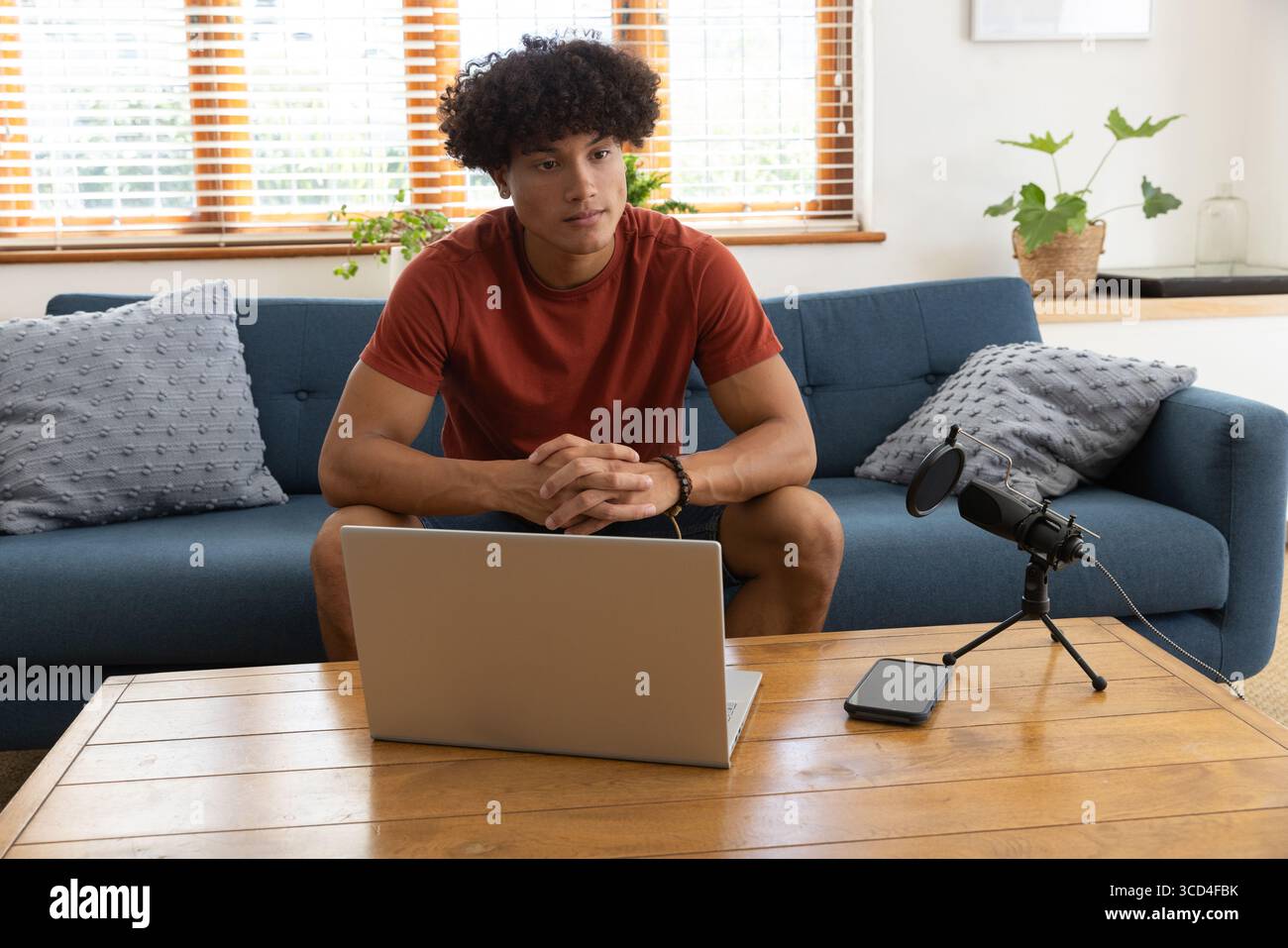 Homme afro-américain assis sur un canapé à la maison enregistrant l'audio avec smartphone portable et microphone Banque D'Images