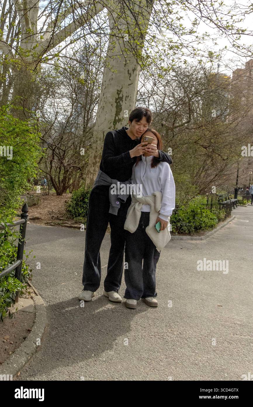 Vue sur la rue d'un couple partageant un téléphone à Central Park, Manhattan, New York, États-Unis, capturant la vie urbaine décontractée et les moments de parc Banque D'Images