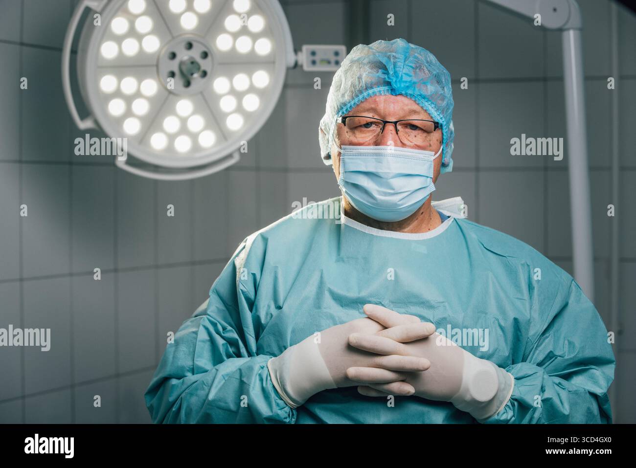 Chirurgien expérimenté dans les gommages bleus et le masque, se tient en toute confiance dans la salle d'opération moderne, éclairé par des lumières chirurgicales brillantes, mettant en valeur la profession Banque D'Images