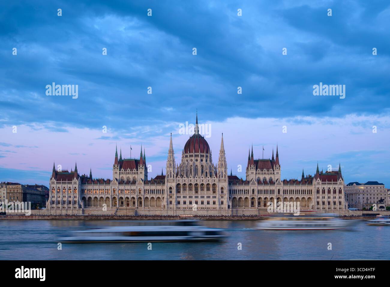 Le majestueux bâtiment du Parlement hongrois se dresse le long du Danube alors que le ciel passe au crépuscule. Les bateaux glissent devant, reflétant l'emblématique Banque D'Images