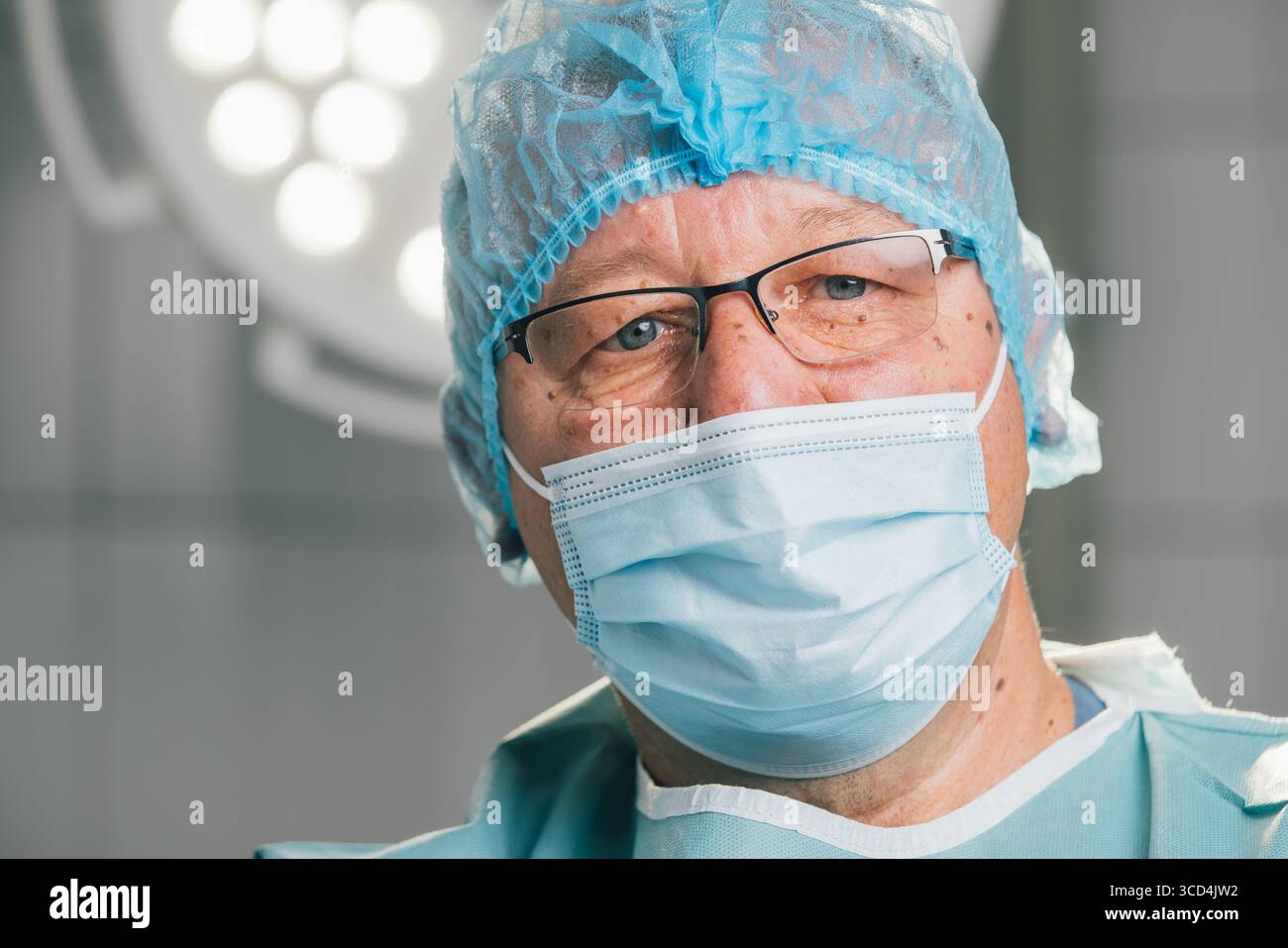 Chirurgien dans la casquette chirurgicale bleue et le masque, se tient dans la salle d'opération, entouré de lumières chirurgicales brillantes, soulignant l'engagement à la sécurité du patient et salut Banque D'Images