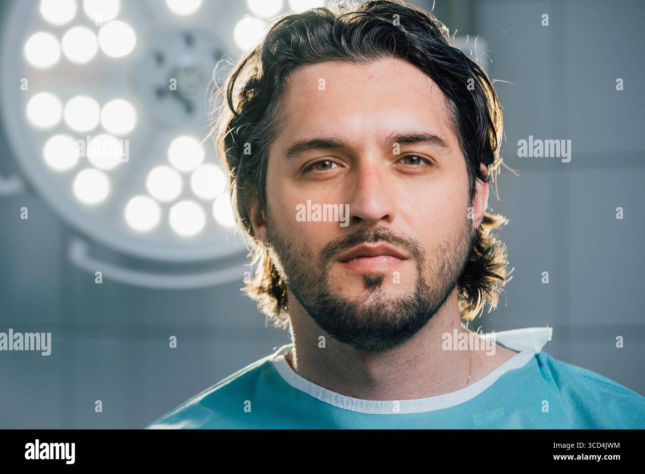 Chirurgien masculin dans des gommages verts, pose dans une salle d'opération, entouré d'équipements médicaux de pointe et de lumières chirurgicales brillantes, incarnant l'engagement envers Banque D'Images