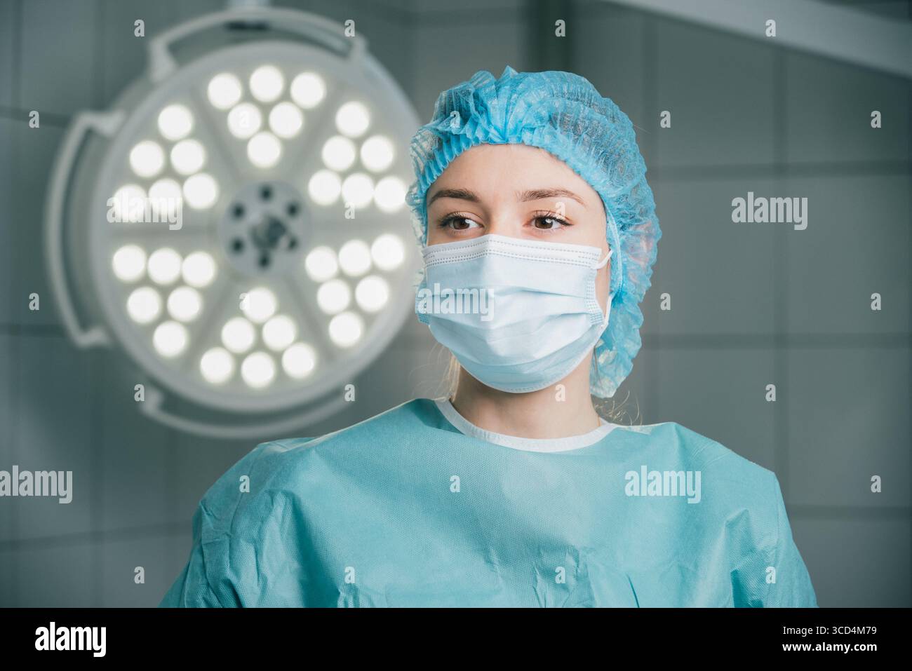 Chirurgienne en tenue chirurgicale bleue et masque, se tient dans une salle d'opération, éclairée par des lumières chirurgicales brillantes, incarnant le professionnalisme et la rea Banque D'Images