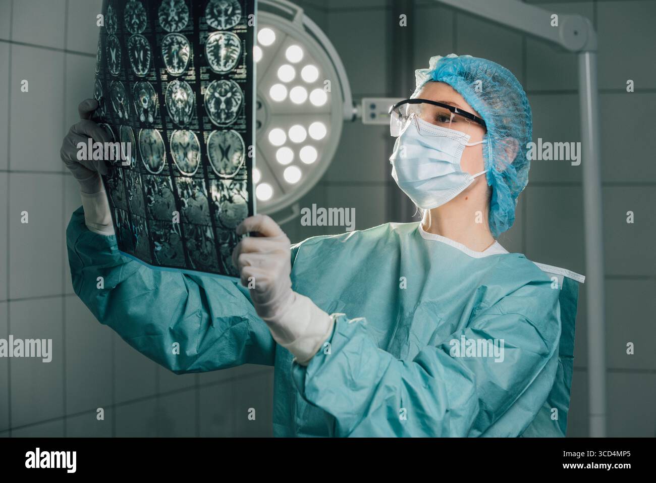 Chirurgien en équipement de protection analyse de près l'imagerie médicale dans une salle d'opération, entouré de lumières chirurgicales brillantes, mettant l'accent sur le R critique Banque D'Images