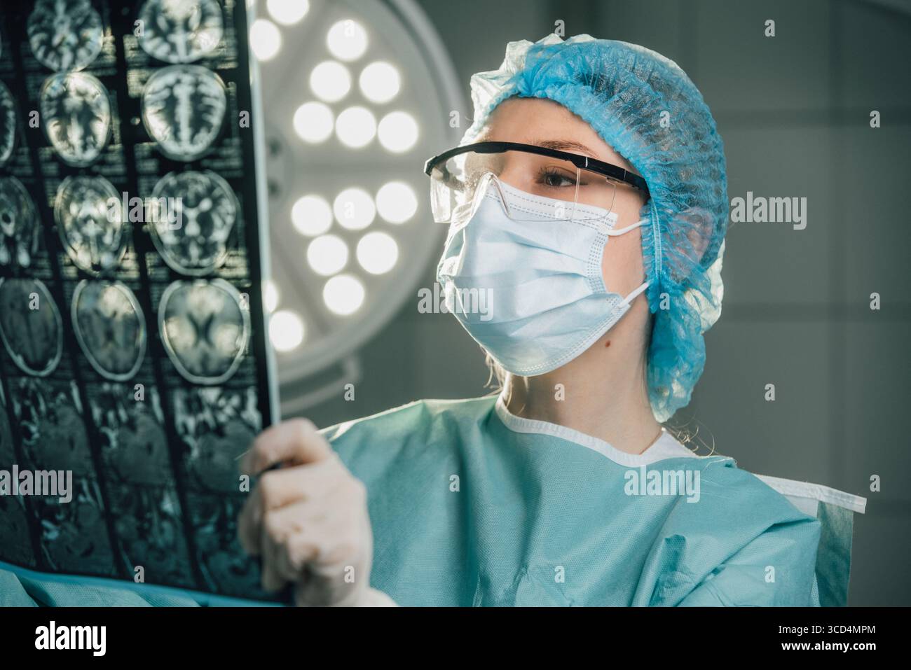 Chirurgien féminin dans les gommages chirurgicaux examine de près l'imagerie médicale dans une salle d'opération, entouré de lumières chirurgicales brillantes, soulignant l'imp Banque D'Images