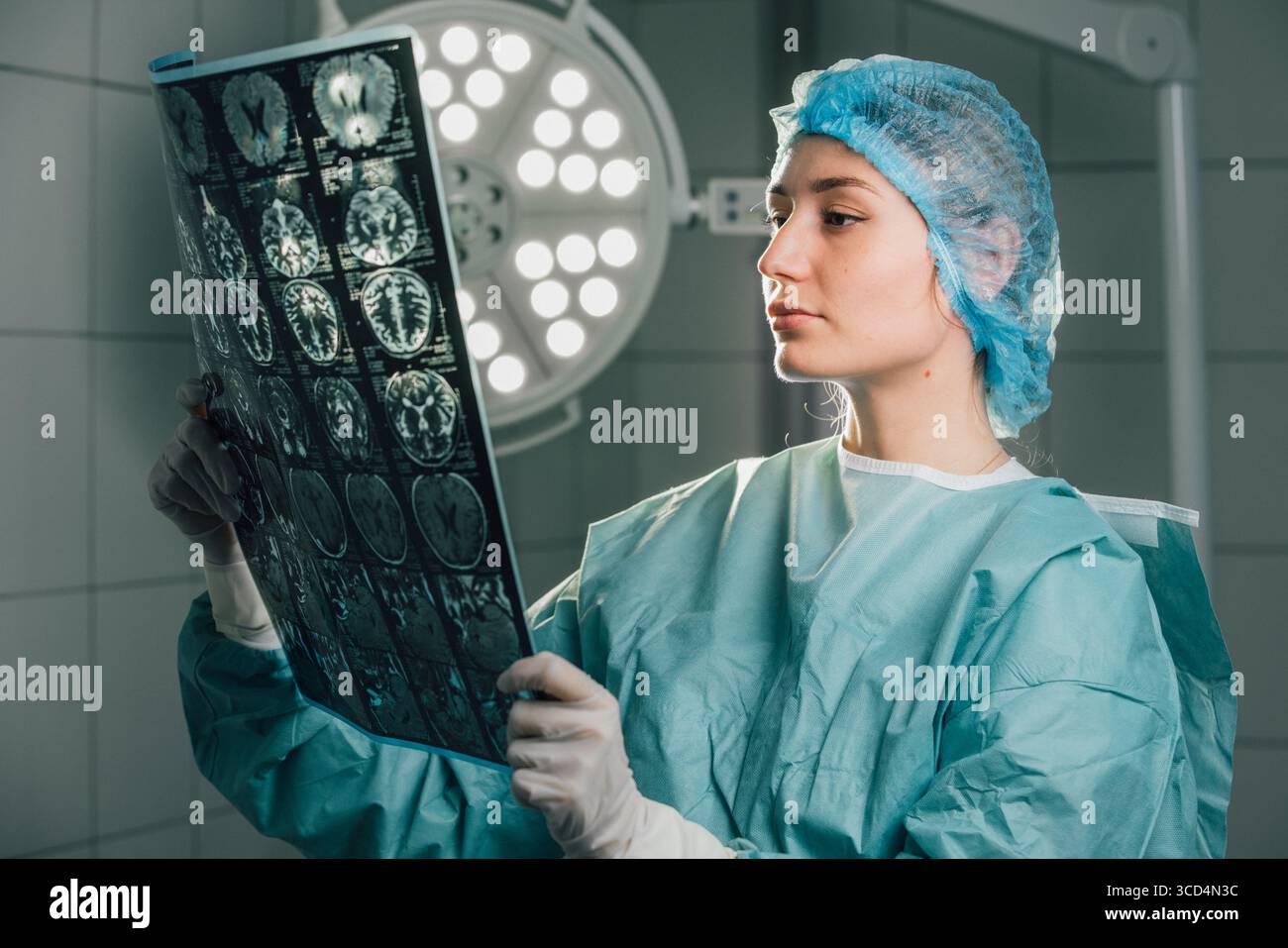 Chirurgien féminin dans les gommages verts, examine l'imagerie médicale dans une salle d'opération, éclairée par des lumières chirurgicales brillantes, démontrant son engagement à Banque D'Images