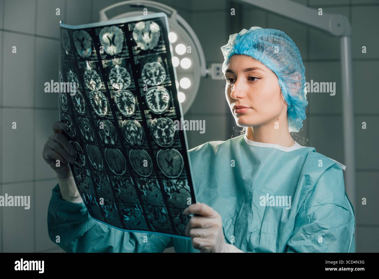 Une femme chirurgienne dans les gommages chirurgicaux analyse des images de scintigraphie cérébrale dans une salle d'opération, sous des lumières chirurgicales brillantes, démontrant son engagement envers le patient Banque D'Images