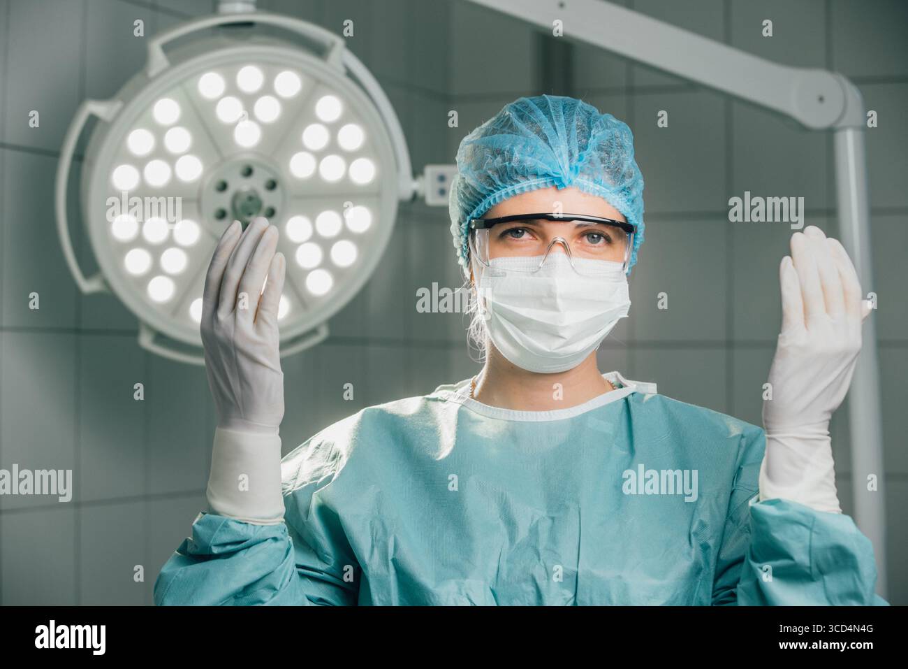 Chirurgien en tenue stérile, portant des gants et un masque, se prépare à la chirurgie dans une salle d'opération moderne avec des lumières vives et un environnement propre emp Banque D'Images