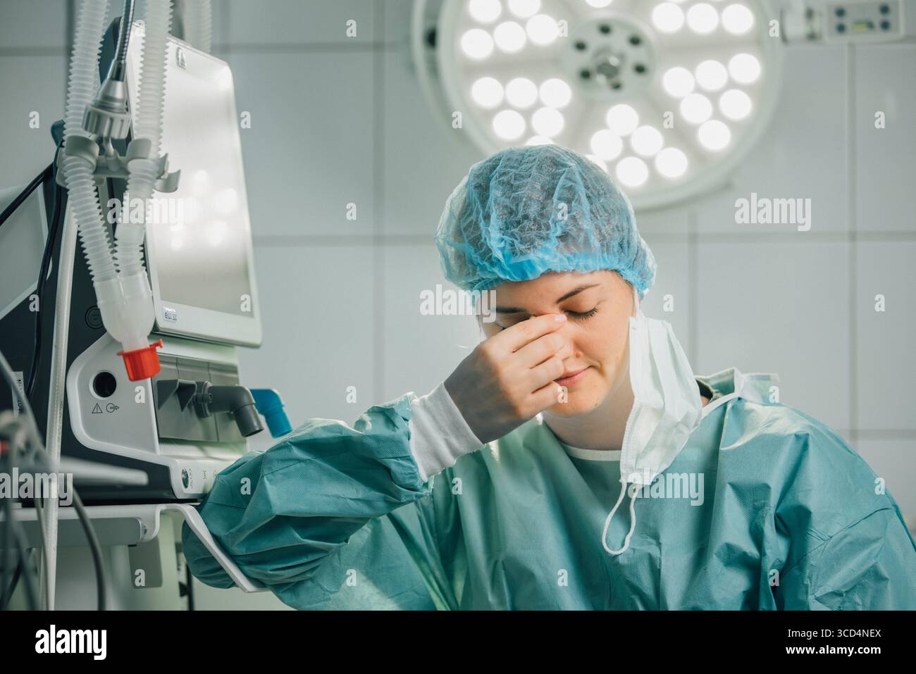 Chirurgien en gommages verts et bonnet chirurgical, montre des signes de stress dans une salle d'opération, entouré d'un équipement médical avancé et d'une lèvre chirurgicale brillante Banque D'Images