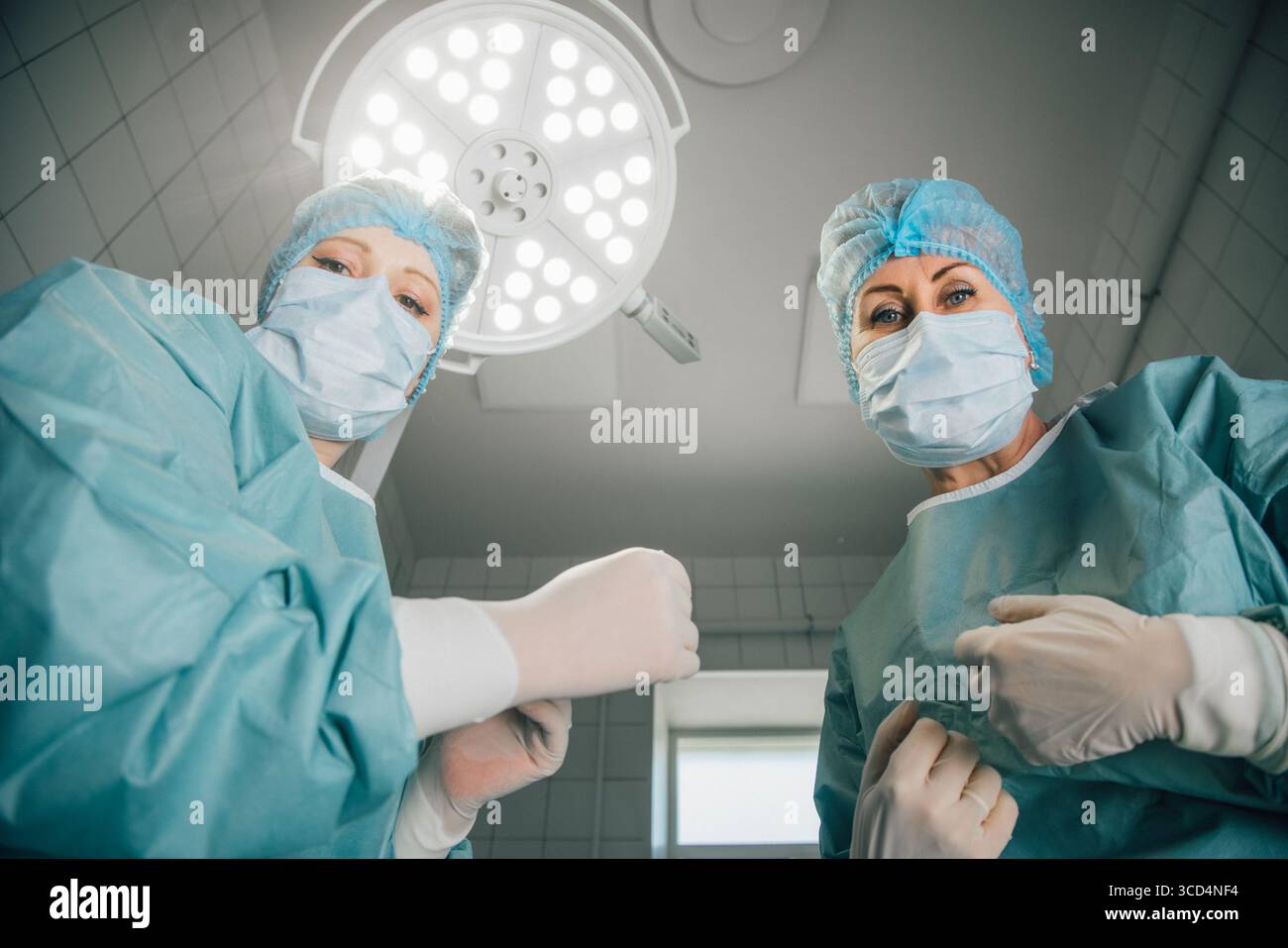 Deux femmes chirurgiennes dans les gommages et les masques, sont prêtes pour la chirurgie sous des lumières vives, mettant l'accent sur la collaboration et le dévouement dans une opération stérile ro Banque D'Images