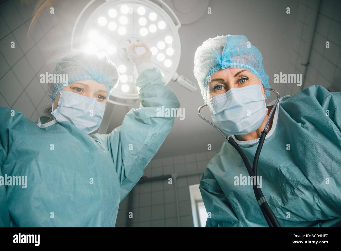 Deux femmes chirurgiennes en gommages et masques, se préparent à la chirurgie sous les lumières lumineuses de la salle d'opération, mettant l'accent sur la collaboration et le dévouement dans un M. Banque D'Images
