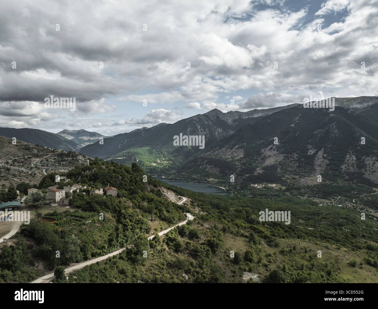 Vue aérienne de l'ancien village accroché à la colline, une tapisserie de pierre et de vert surplombant le lac tranquille et les montagnes lointaines, Frattura Vecchia, Scanno, Abruzzes, Italie. Banque D'Images