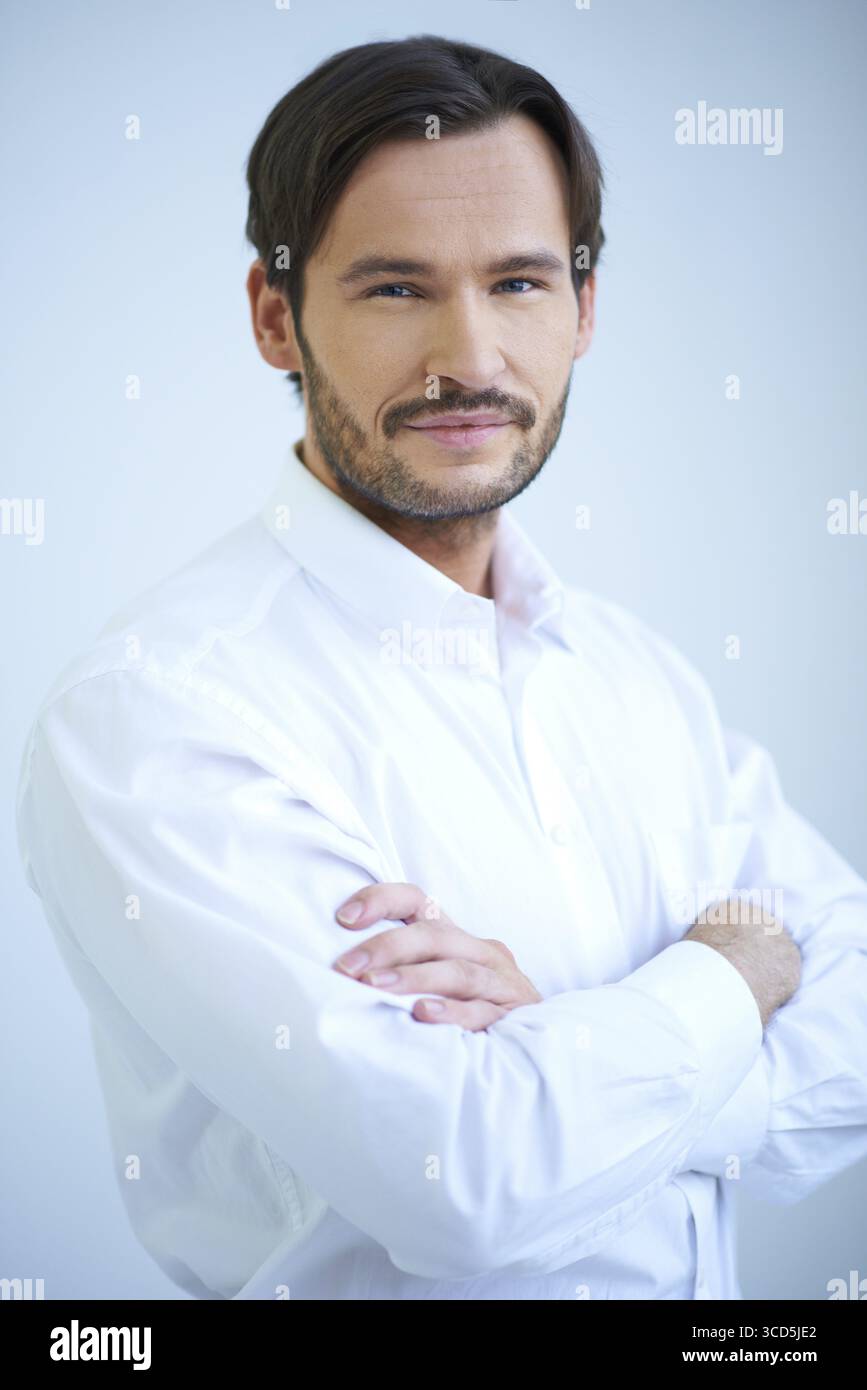 Attrayant homme barbu souriant en manches courtes debout avec ses bras pliés, haut du corps portrait studio sur blanc Banque D'Images