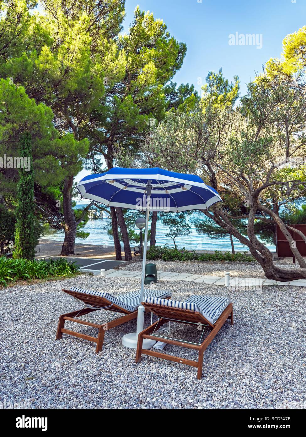 Deux chaises longues vides avec un parasol bleu sur une plage de galets, offrant un endroit tranquille pour la détente avec une belle vue sur la mer.Une détente parfaite Banque D'Images