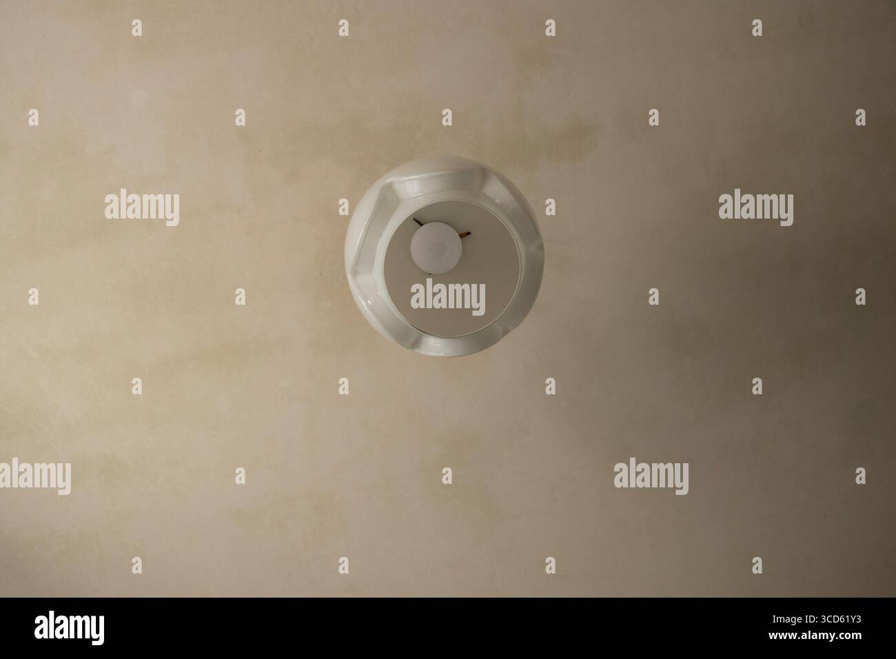 Plafonnier avec un abat-jour rond blanc et une ampoule dans une pièce avec de vieilles réparations et du plâtre lumineux dans un appartement Banque D'Images