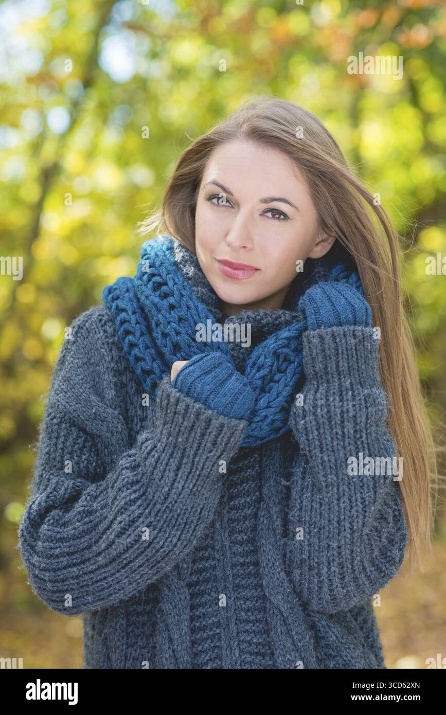 Femme à la mode chaude de l'automne se blottissant dans son maillot bleu à col polo et son foulard tout en marchant à l'extérieur dans un parc Banque D'Images