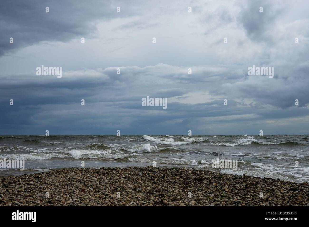 Plage de galets et vagues de la mer Baltique sous un ciel couvert d'humeur sombre. Banque D'Images