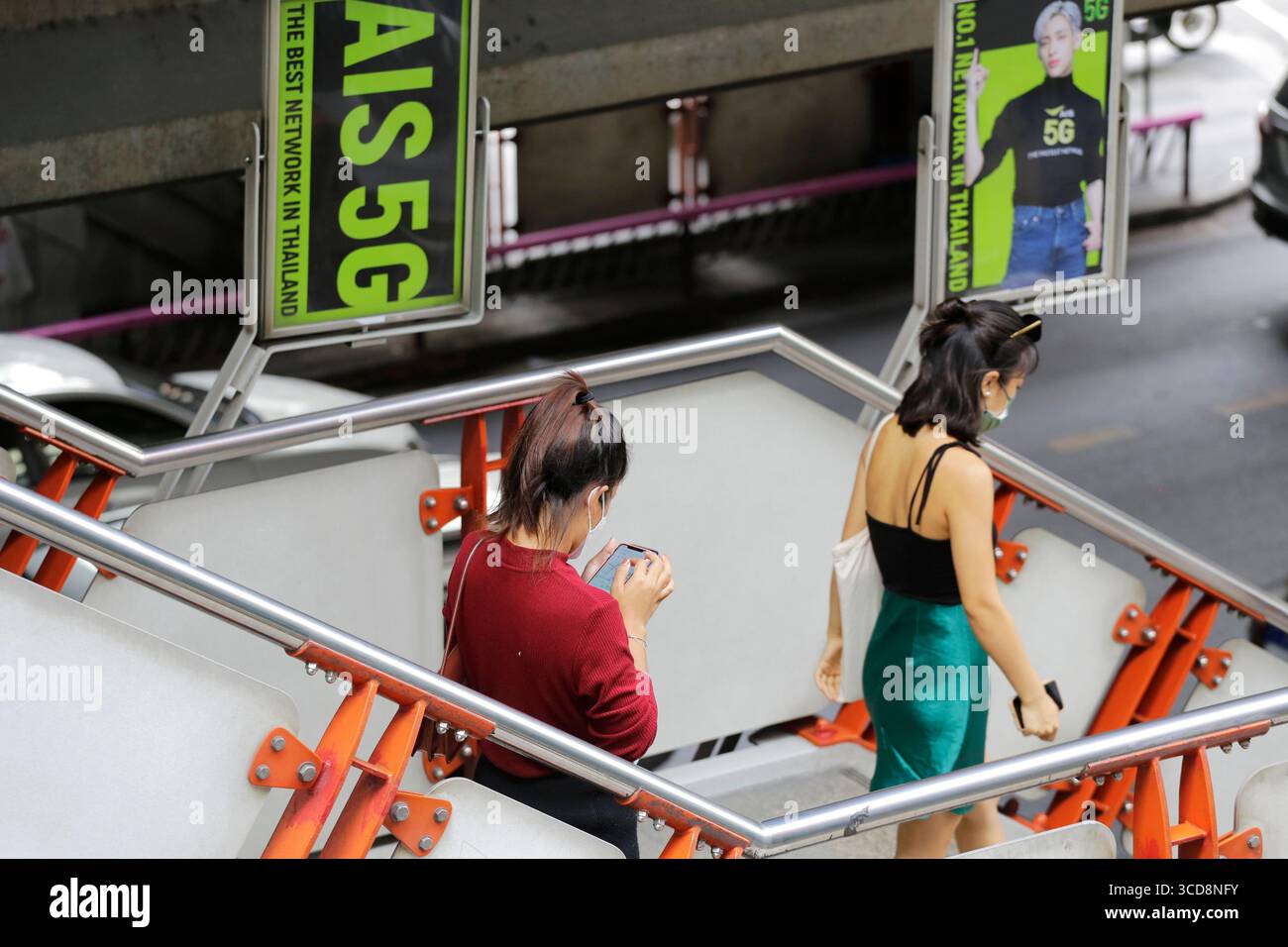 Bangkok, Thaïlande - 4 juillet 2022 : une femme vérifie son téléphone portable à côté d'une publicité AIS, une compagnie thaïlandaise de téléphonie mobile. Banque D'Images