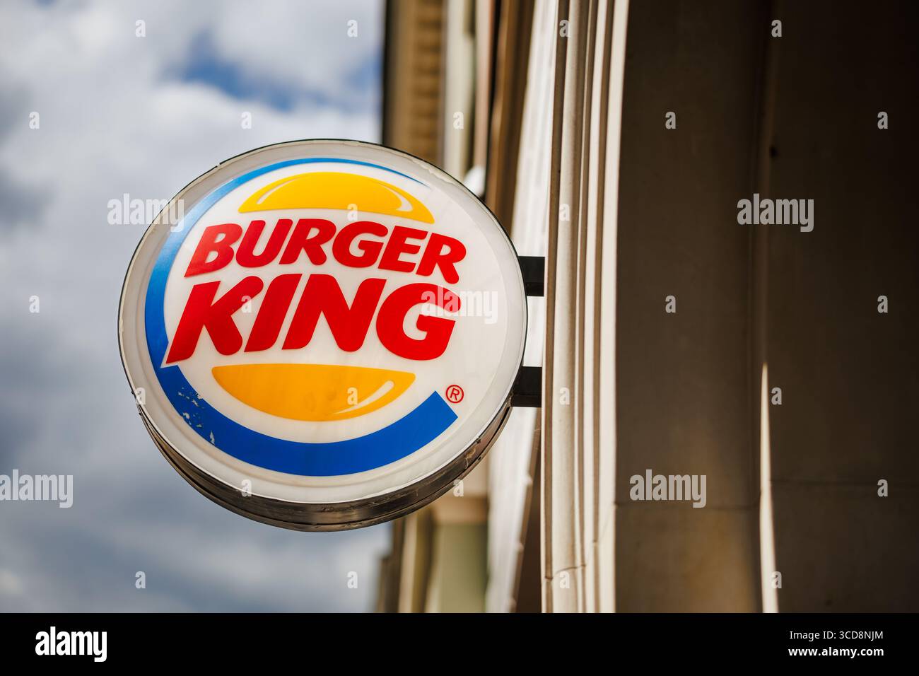 Logo Burger King attaché à la façade d'un bâtiment, avec un ciel nuageux en arrière-plan. Banque D'Images