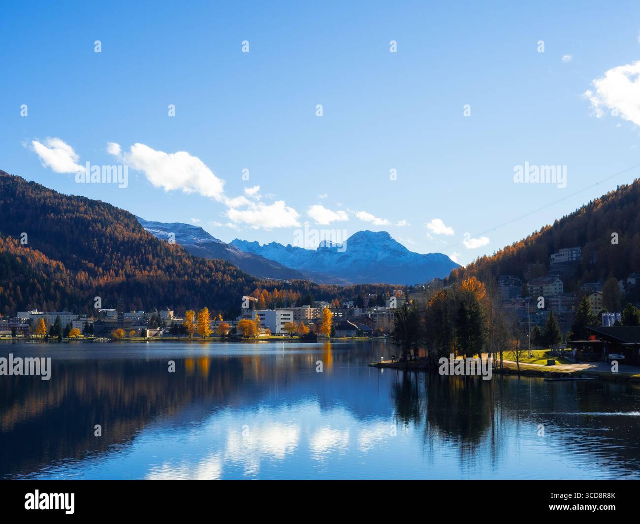 Vue panoramique sur le lac de Moritz avec arbres d'automne, reflets sur l'eau, et montagnes enneigées en arrière-plan, Engadine, Suisse. Banque D'Images