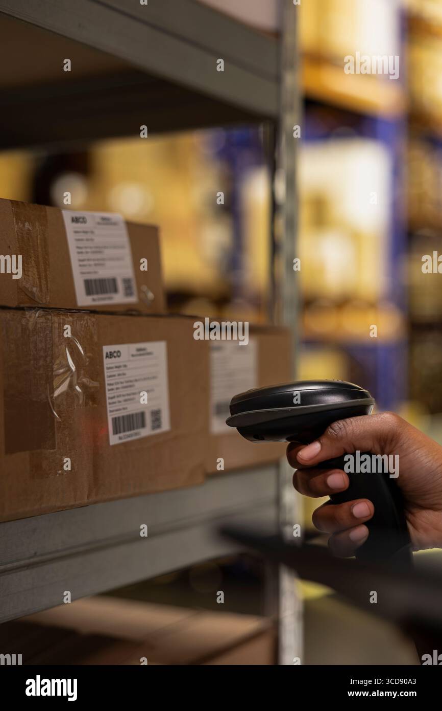 Gros plan d'un travailleur d'un dépôt industriel scannant les détails des colis à l'aide d'un logiciel de suivi, marchant près d'énormes racks de stockage. Le système de gestion de livraison de commerce électronique assure la précision dans le traitement des commandes. Banque D'Images