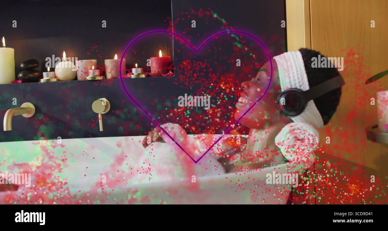 Femme inclinée portant une serviette écoutant à travers des écouteurs dans la baignoire avec oreiller en mousse et bougies allumées Banque D'Images