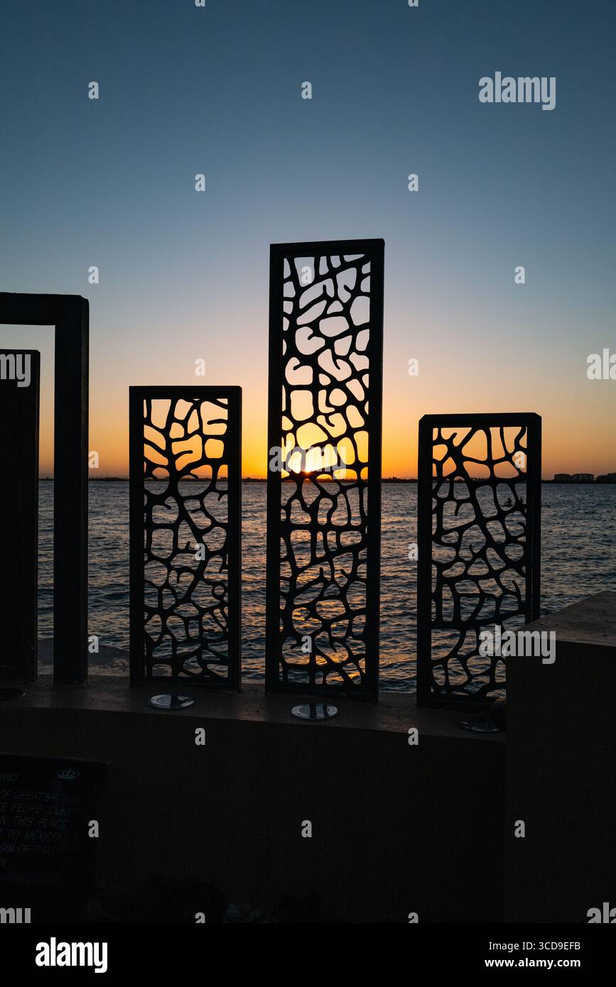 Présentoir lumineux avec plaques métalliques devant l'océan avec soleil couchant. Banque D'Images