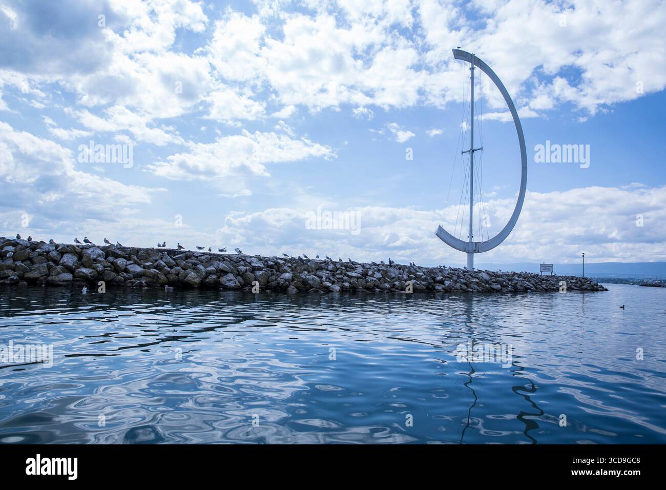 Monument moderne en forme de croissant sur un brise-lames rocheux au bord de l'eau d'Ouchy le long du lac Léman sous un ciel bleu ensoleillé. Banque D'Images