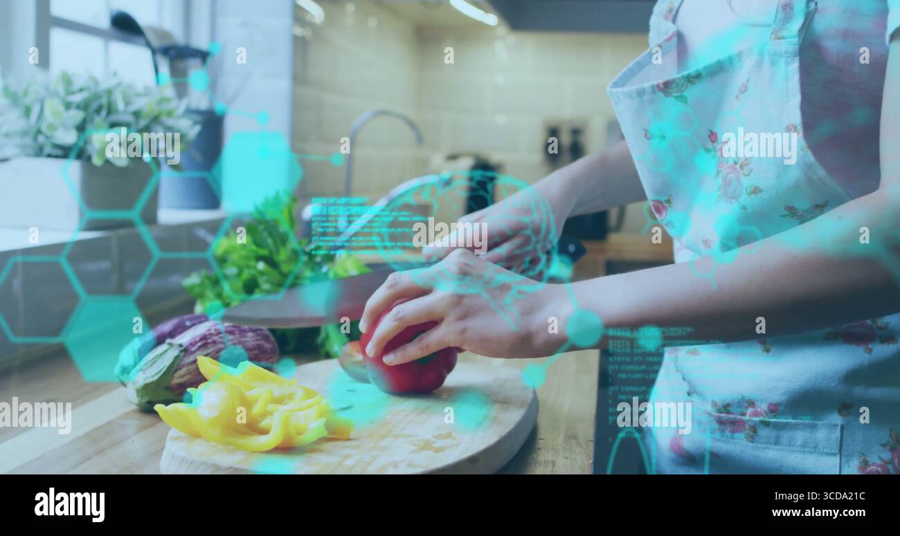 Femme portant un tablier floral hachant le poivron rouge dans la cuisine, avec planche à découper et recouvrement AR Banque D'Images