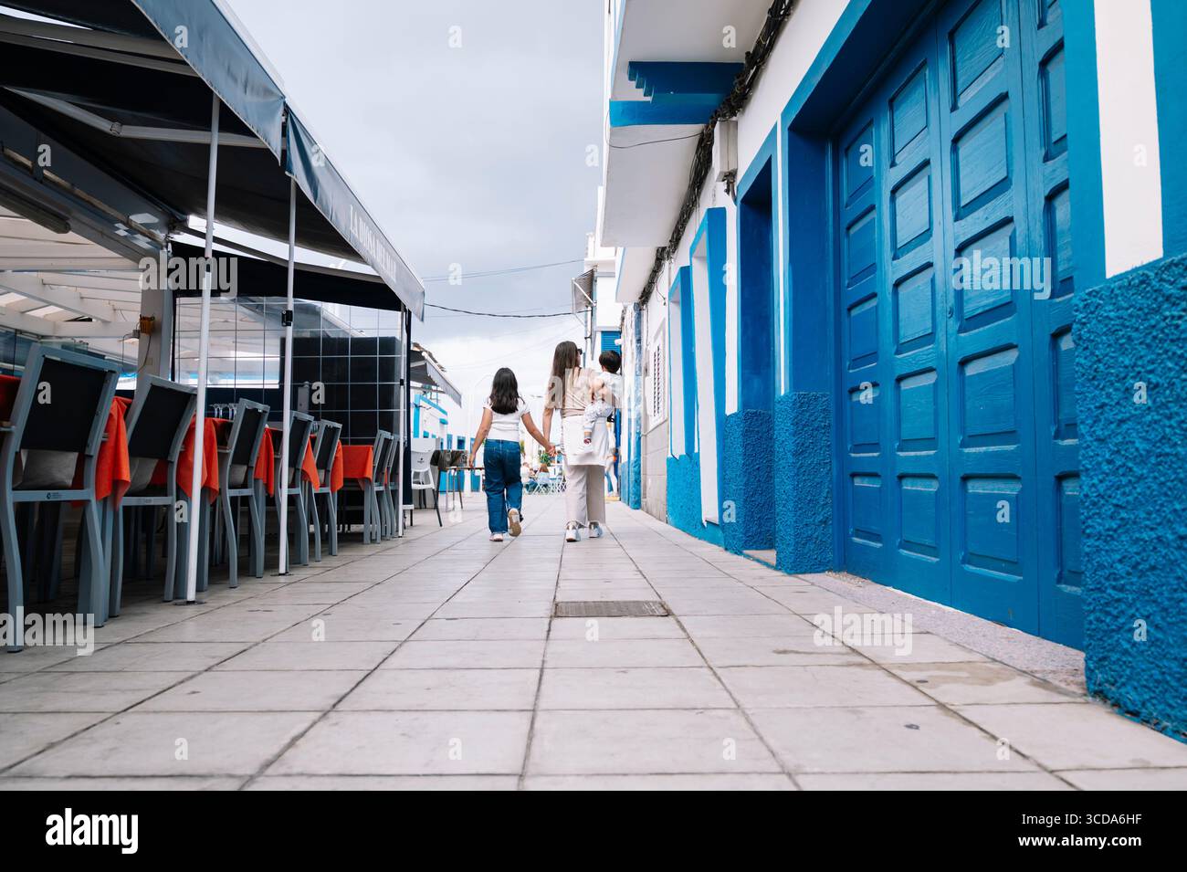 Une femme et deux enfants marchent dans une rue devant un bâtiment bleu à Agaete Gran Canaria. La scène est animée et joyeuse, avec les enfants ho Banque D'Images