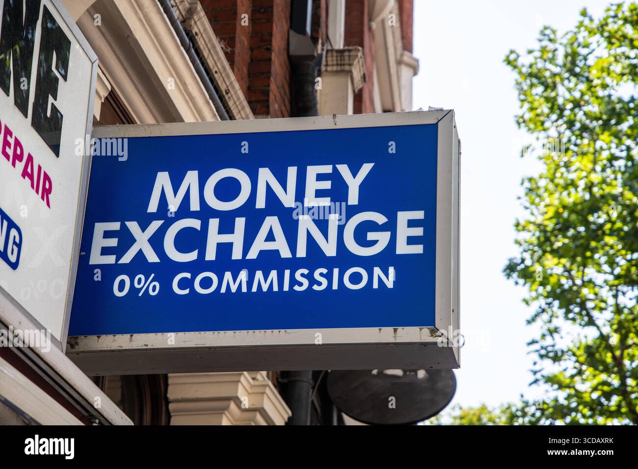 Enseigne bleue “Money Exchange – 0% Commission” en lettres blanches, montée au-dessus d’un magasin, offrant des services de change. Banque D'Images