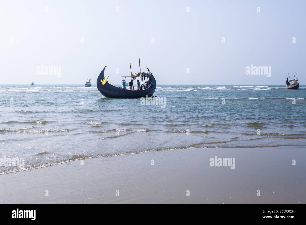 Cox's Bazar, Bangladesh - 04 février 2024 : vue de bateaux de pêche traditionnels qui bondissent doucement sur les vagues turquoises chatoyantes près de la côte sablonneuse. Banque D'Images