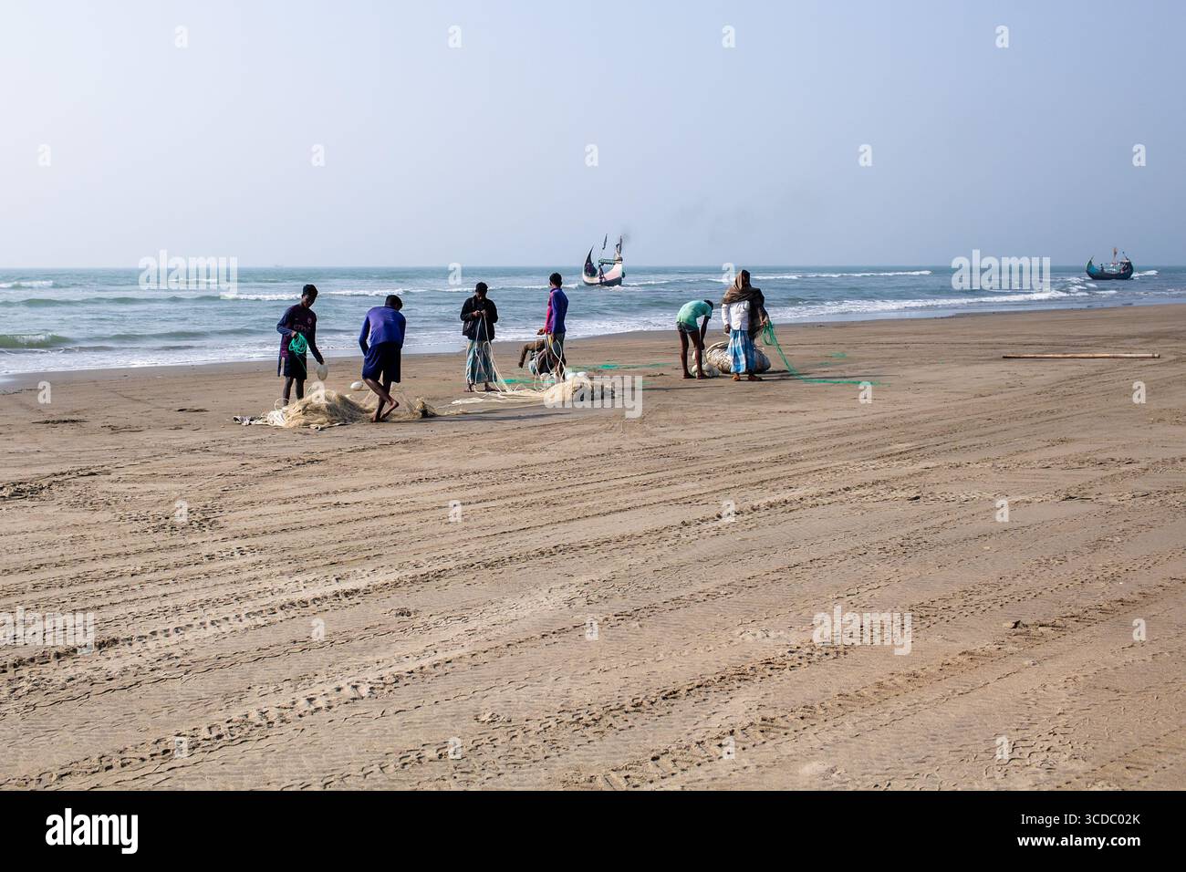 Cox's Bazar, Bangladesh - 04 février 2024 : vue de pêcheurs tirant des filets sur le sable doré de la plage de Cox's Bazar sous un ciel pâle, leurs silhouettes se silhouant contre l'horizon de l'océan. Banque D'Images