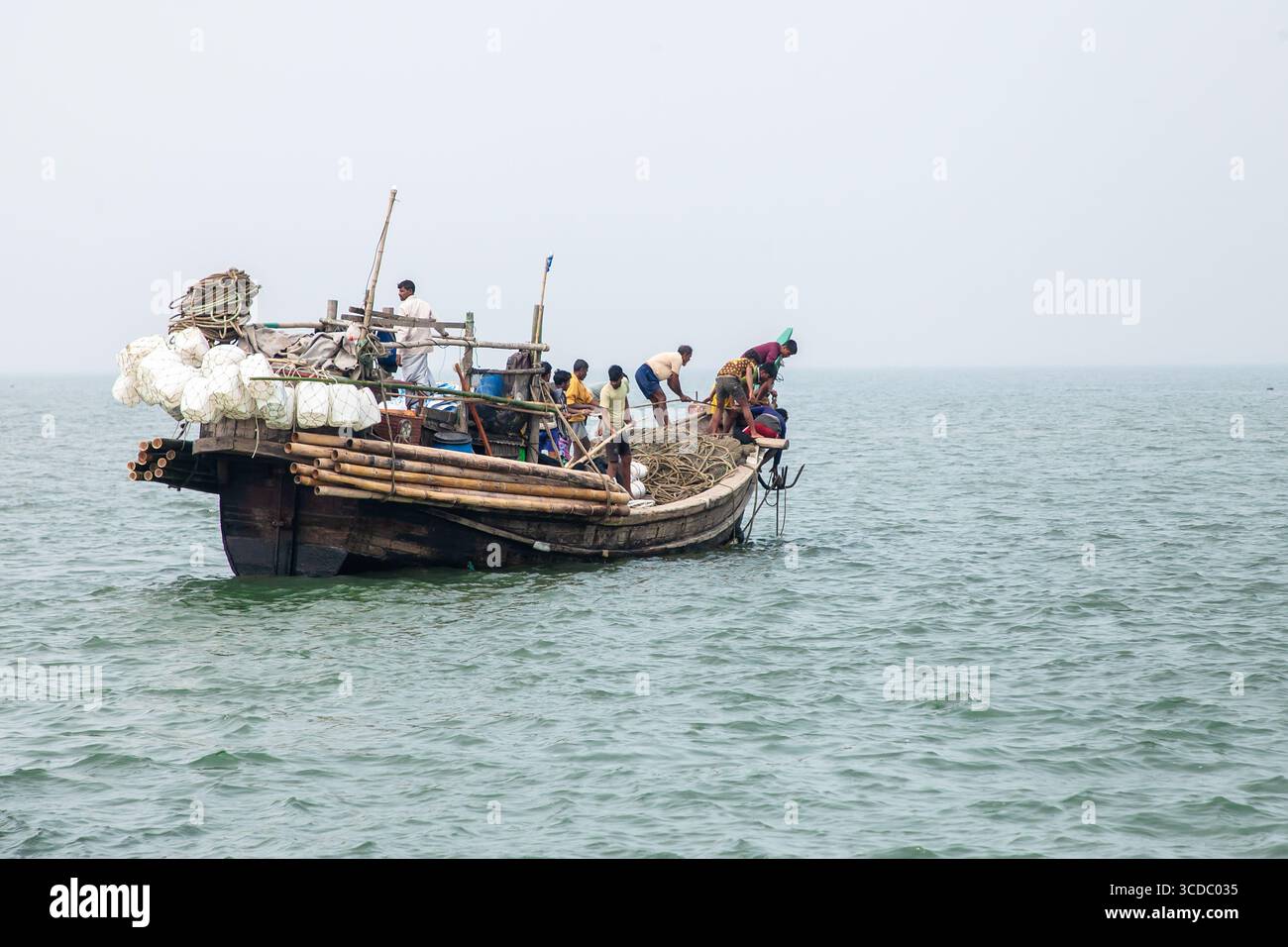 Cox's Bazar, Bangladesh - 07 février 2024 : vue du bateau de pêche naviguant sur la mer avec des pêcheurs travaillant, sous un ciel pâle, près de Cox's Bazar - Teknaf Highway. Banque D'Images