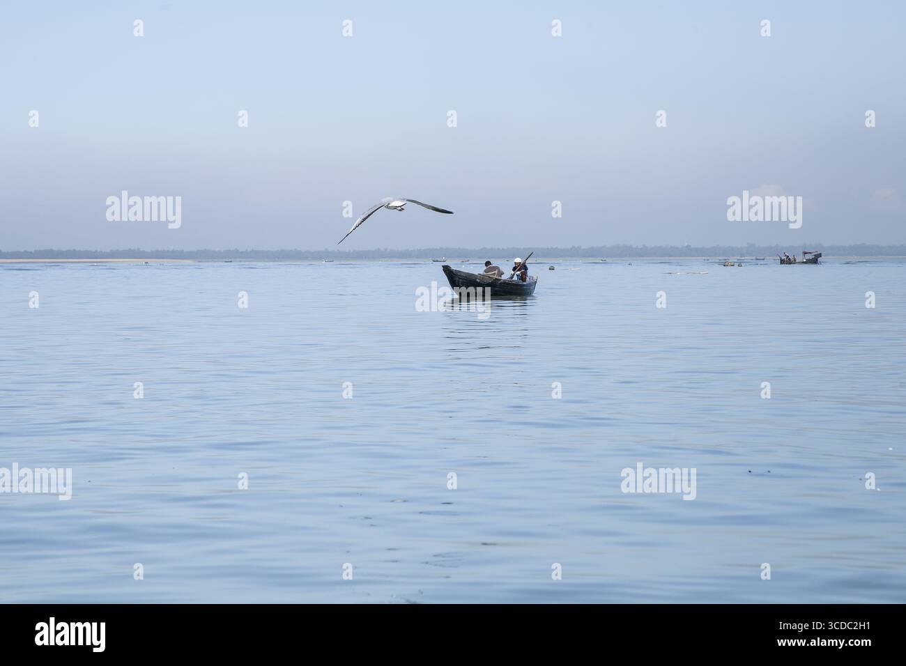 Cox's Bazar, Bangladesh - 29 novembre 2022 : vue d'un petit bateau de pêche planant sur les eaux calmes et bleues pâles tandis qu'une mouette seule vole au-dessus de la tête, créant une scène côtière sereine. Banque D'Images