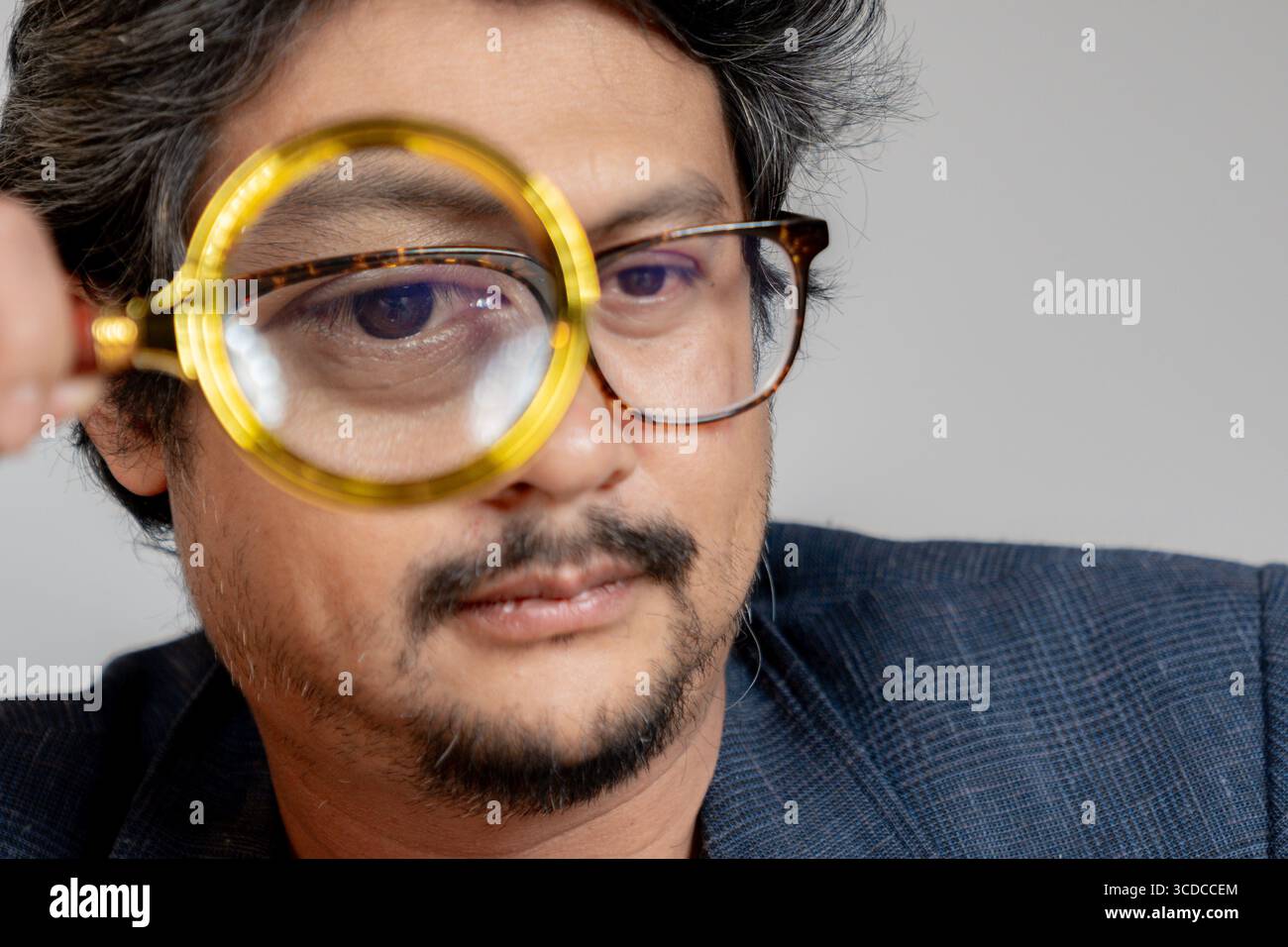 Un jeune homme lisant un livre avec une loupe, symbolisant la concentration et l'étude détaillée. Banque D'Images