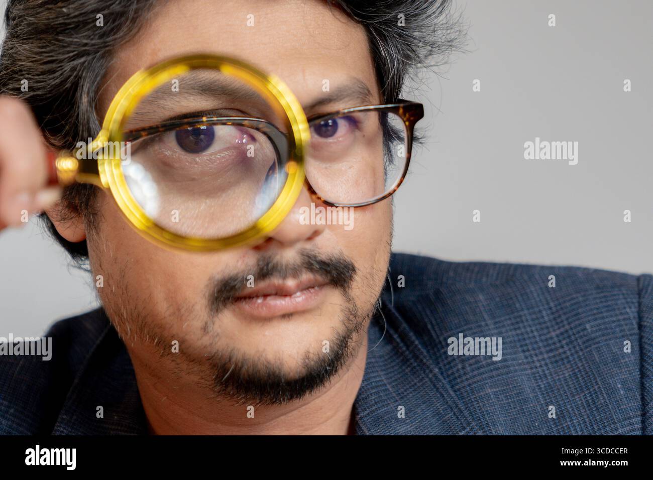 Un jeune homme lisant un livre avec une loupe, symbolisant la concentration et l'étude détaillée. Banque D'Images