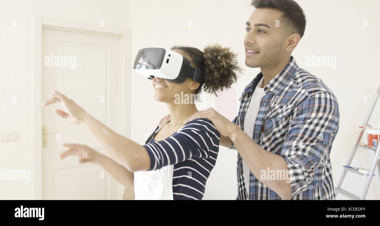 Femme dans des combinaisons et des lunettes de réalité virtuelle reçoit l'aide de son mari Banque D'Images