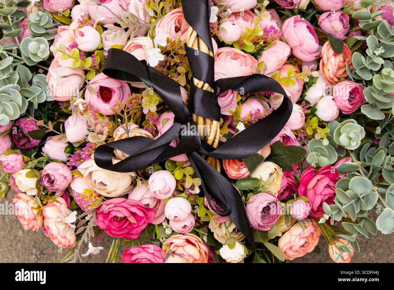 Un bouquet de fleurs artificielles roses, blanches et Bordeaux avec feuillage vert dans un panier avec un ruban de deuil noir sur la poignée, un bouquet funéraire Banque D'Images