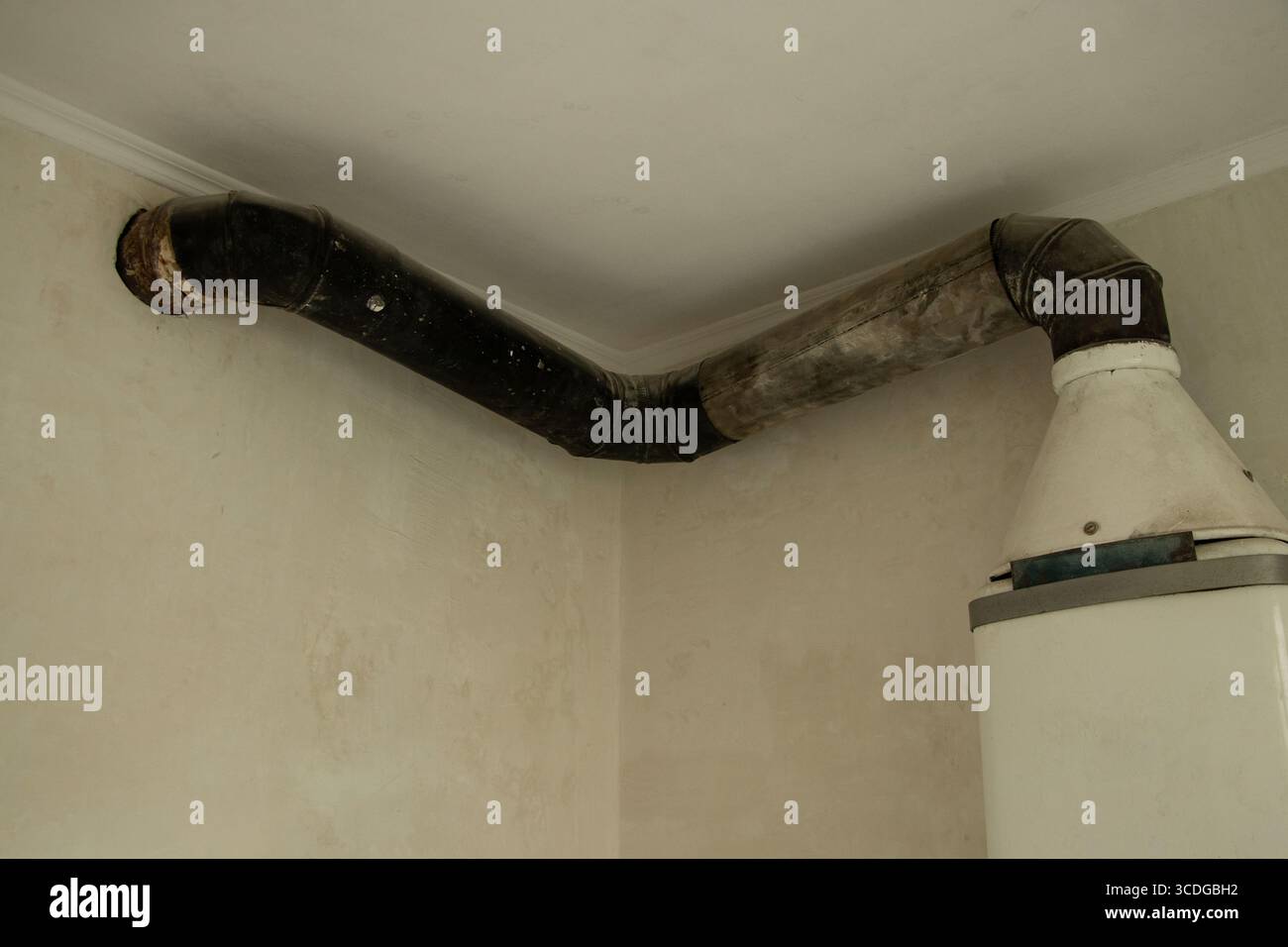 Ancienne chaudière à gaz avec tuyau de ventilation en métal dans le coin de la pièce sur le mur blanc lors de la rénovation de la maison Banque D'Images