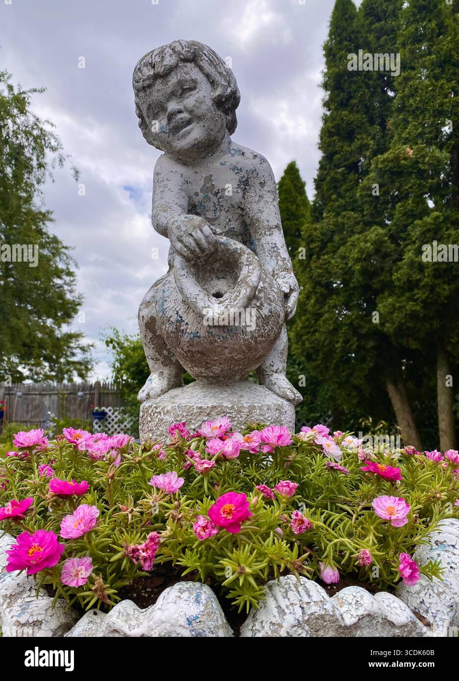 Statue d'un enfant avec une aiguière positionnée au-dessus de fleurs de portulaca rose vif avec un ciel orageux en arrière-plan - Image de stock capturée avec un smartphone