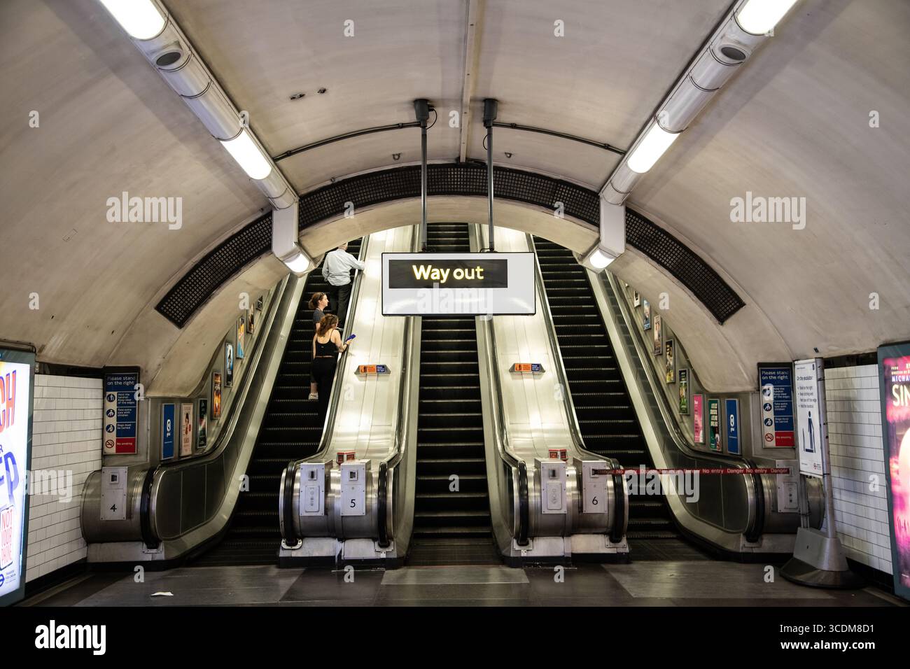 Panneau Way Out sur le métro londonien avec escalator en arrière-plan, symbolisant la sortie, la direction du voyage et le design emblématique des transports britanniques. Banque D'Images