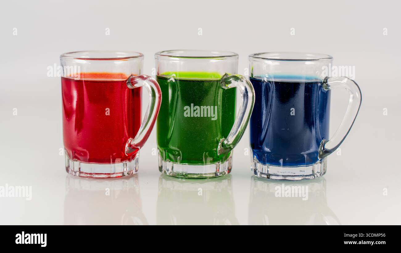 Trois tasses en verre remplies de boissons colorées rouges, vertes et bleues sur fond blanc Banque D'Images