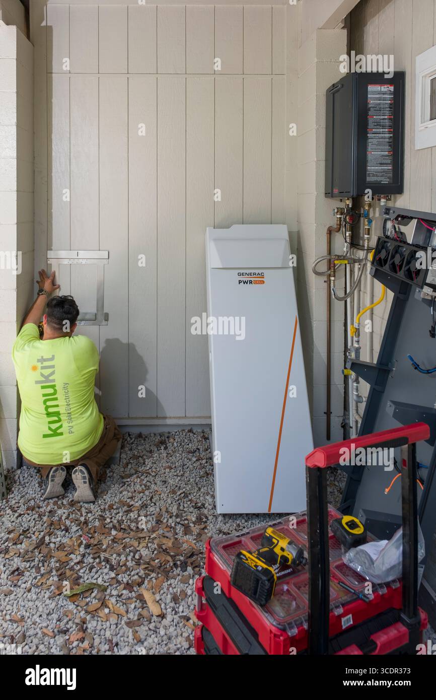Jeune homme installant un support mural pour l'armoire de batterie Generac PWRcell lors d'une installation photovoltaïque résidentielle, Honolulu, Oahu, Hawaii, Etats-Unis Banque D'Images