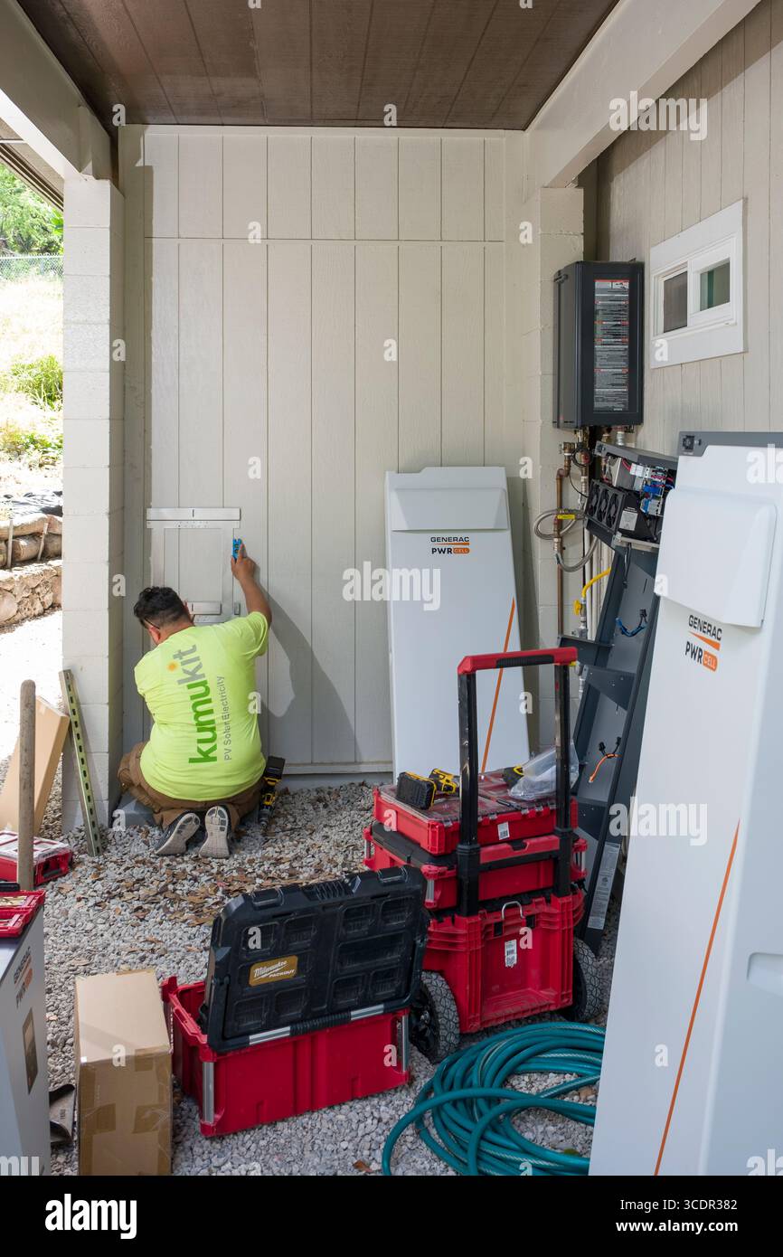 Jeune homme installant un support mural pour l'armoire de batterie Generac PWRcell lors d'une installation photovoltaïque résidentielle, Honolulu, Oahu, Hawaii, Etats-Unis Banque D'Images