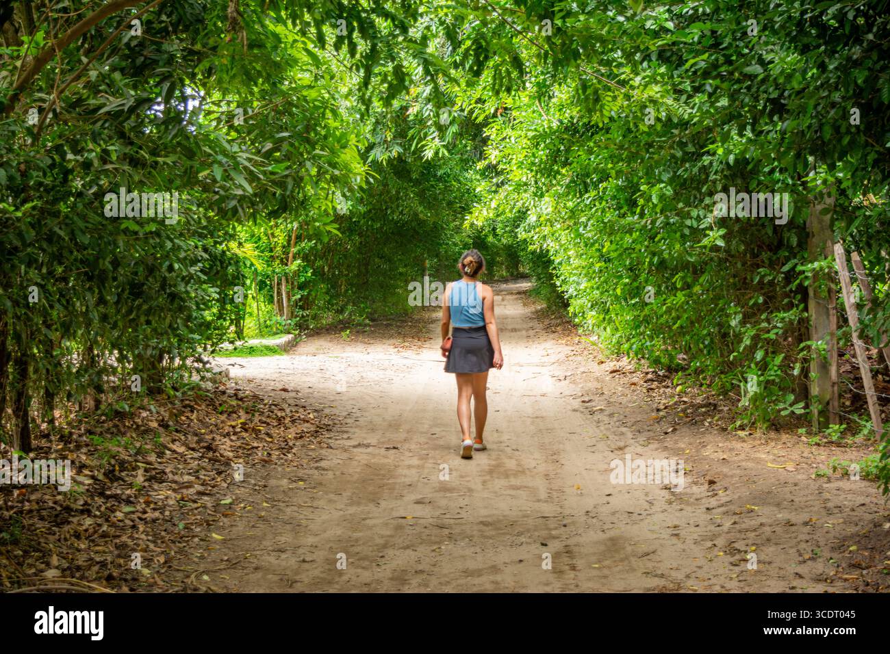 Une femme marche le long d'un sentier serein de terre entouré d'un feuillage vert luxuriant à Palomino, la Guajira, Colombie. Banque D'Images