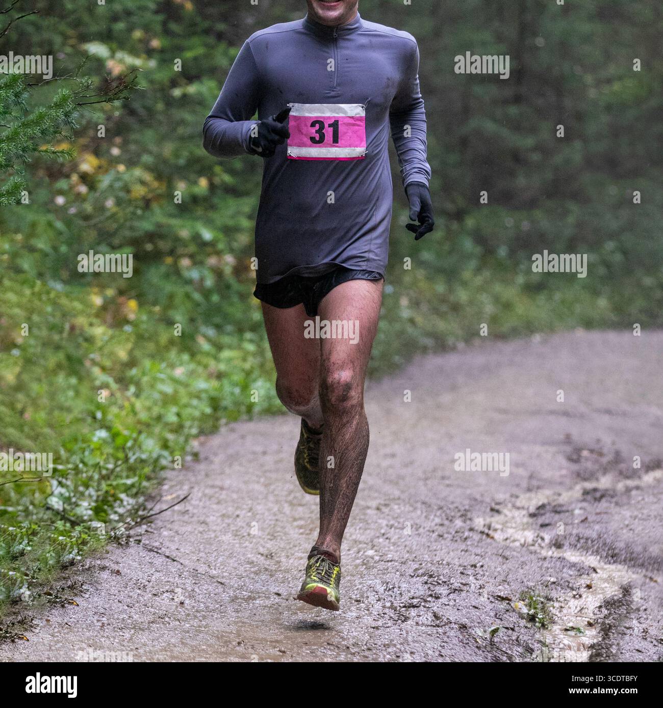 Coureur en bavoir numéroté courir sur un sentier en forêt boueuse pendant le marathon Banque D'Images