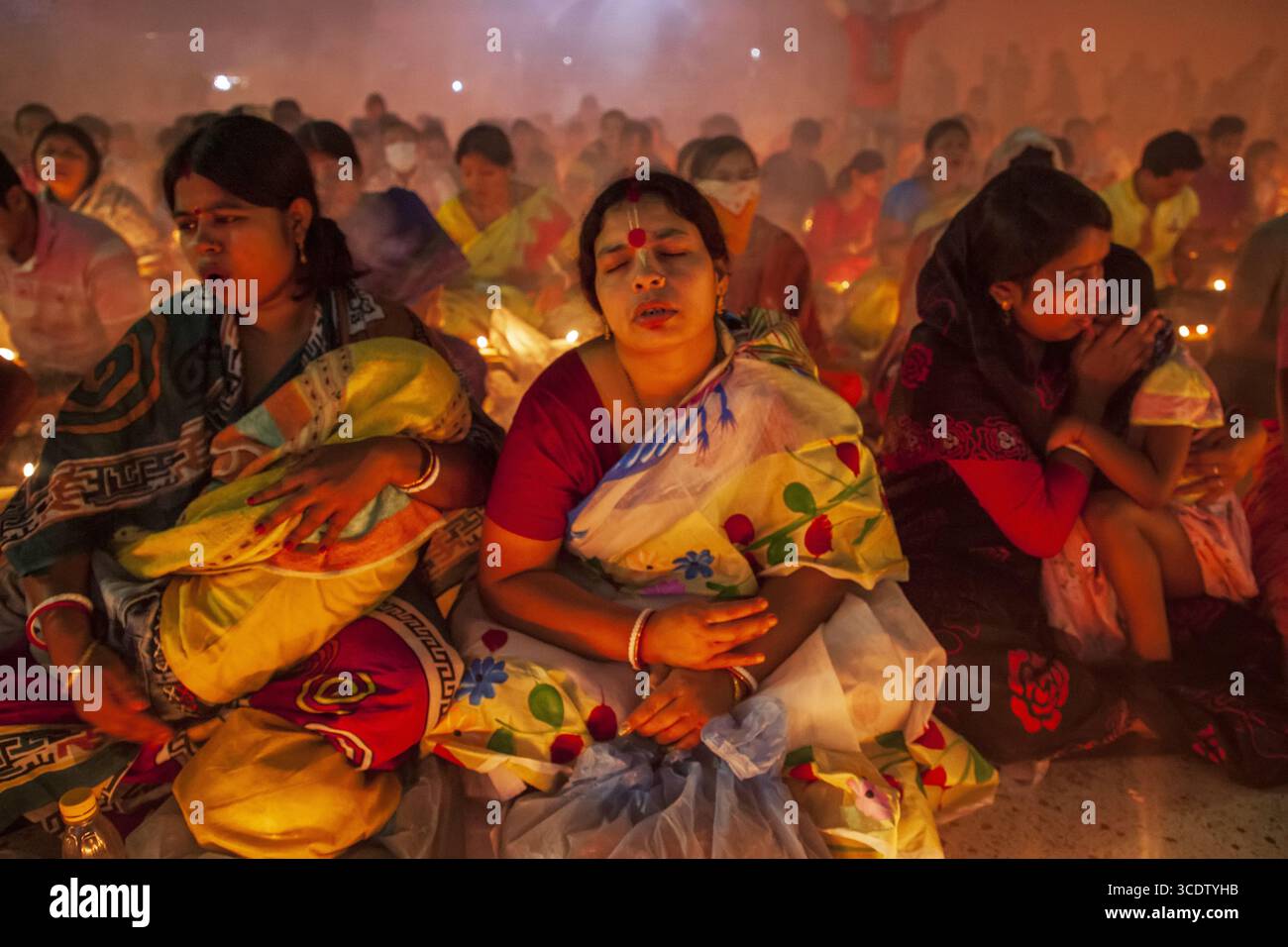 Narayanganj, Bangladesh - 15 novembre 2022 : vue de femmes en saris colorés, têtes inclinées dans une prière solennelle, illuminées par la douce lueur des bougies. Banque D'Images