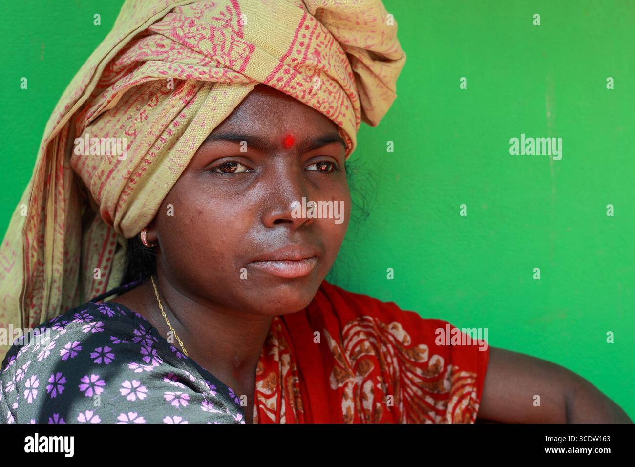 Sitakund, Bangladesh - 21 février 2020 : la vue d'une femme à la peau foncée, ornée d'un turban à motifs et d'un bindi rouge traditionnel, se distingue sur un fond vert éclatant. Banque D'Images