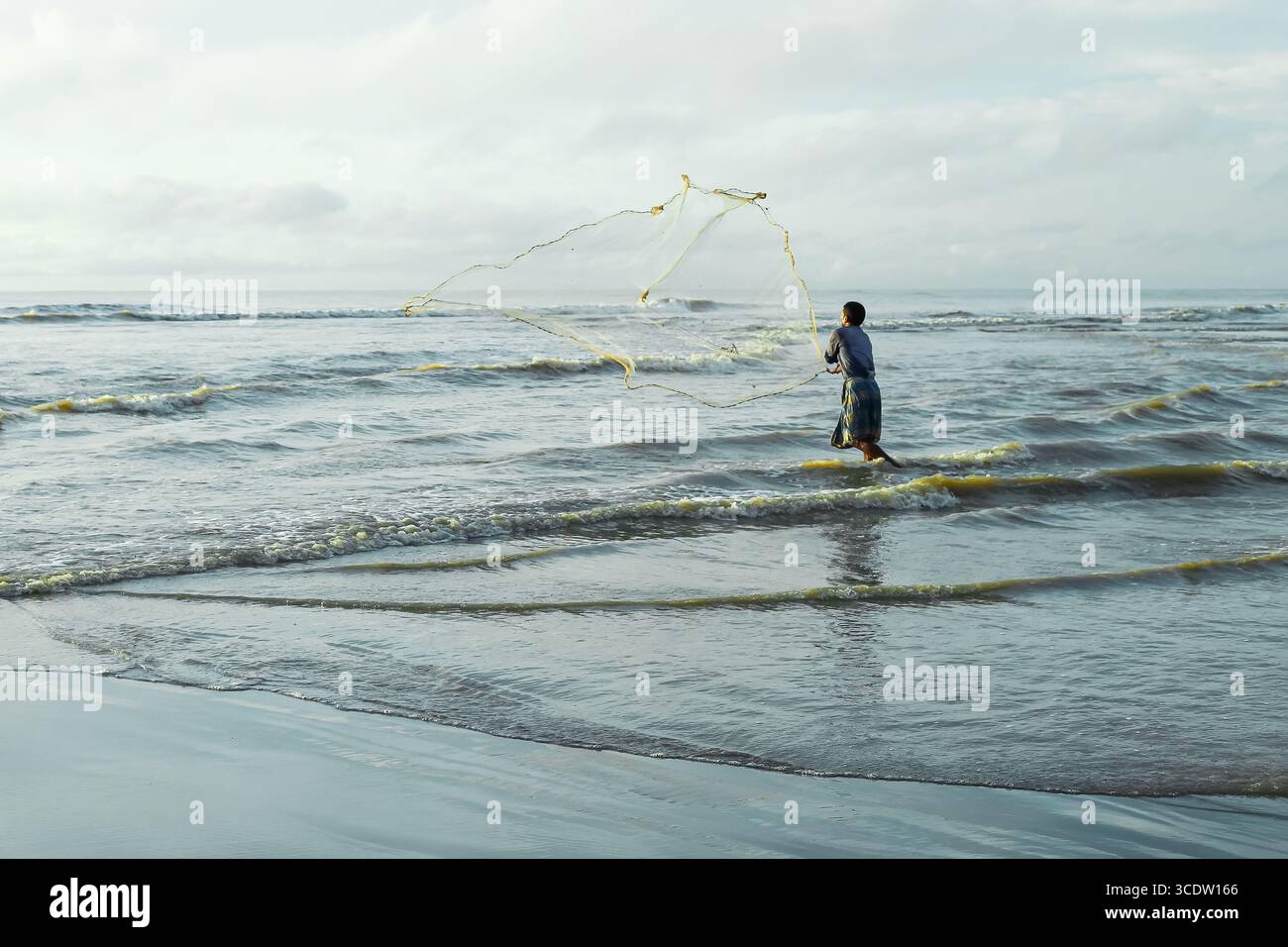 Cox's Bazar, Bangladesh - 11 octobre 2019 : vue d'un pêcheur solitaire jetant son filet dans la mer tranquille et ondulée sous un ciel doux et couvert. Banque D'Images